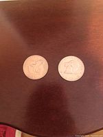 Two silver dollar coins placed side by side on a wooden surface, front side showing the eagle landing on the moon and Liberty Bell designs.