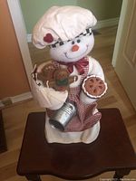 Front view of the plush baking snowman decorated with cookies, pie, and metal bucket.