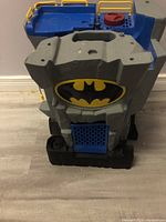 Front view of the Batman Imaginext Batcave playset showing the large black and yellow Bat emblem on gray plastic, with blue and yellow upper sections including dials.