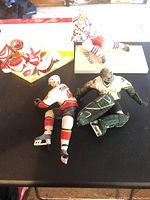 Photo showing four McFarland NHL player figures set on a dark surface. Visible are the details of players' uniforms and bases. Figures lack sticks; Alex Tanguay figure missing one arm.