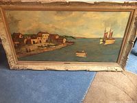 Full view of the large rectangular landscape and seascape painting featuring coastal village and boats, framed in ornate carved frame.
