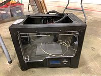 Front and left side view showing black metal frame with clear front door and LCD control screen.