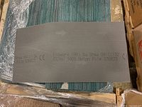 Photo showing a dark solid backing of a carpet piece with printed manufacturer details including 'Economy (PP) By Shaw' and '100% Nylon Pile'.