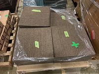 Top view of beige square carpet pieces stacked and wrapped on a pallet with green labels on some pieces showing size marks.