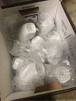 Photo of ceramic mugs wrapped in bubble wrap inside a cardboard box.