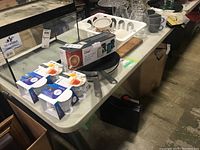 Photo showing white resin folding table with metal legs and various household items on top (not included).