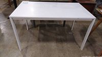 Front view of white rectangular IKEA Melltorp table showing metal legs and laminate top with scratches.