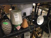 Wide view of seven lamps on black shelf showing ceramic, metal, plastic bases and absence of shades or bulbs