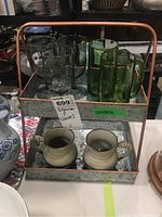 Front view of metal organizer stand on a table holding glass stemware glasses, green glass mugs on top tray, and two pottery mugs on bottom tray
