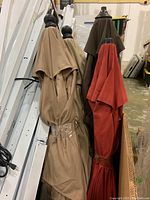 Six patio umbrellas in assorted colors including beige, brown, and red, standing upright in a cardboard box in a warehouse setting.