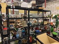 Photo showing three black plastic shelving units with various household items on shelves to illustrate units, in warehouse setting.
