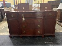 Front view of the wooden sideboard cabinet showing drawers, brass handles, and side cabinet doors, with visible damage near the base.
