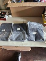Three car trunk liners placed side by side on a table, two still sealed in plastic packaging and one unpackaged.