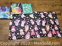 Four folded Animal Crossing themed towels laid on floor showing black towel with pink character prints and three others in packaging