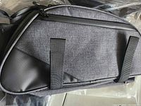 Side view of gray and black bike trunk bag showing fabric texture, zipper, and attachment straps.