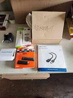 Photo showing Amazon Fire Stick retail box, USB 3.0 cord, power supply, iPod case, selfie stick, and HDMI cables.