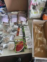 Overview of seed packets including Survival Garden brand and Burpee watermelon seeds, with other gardening packets and accessories on a table surface.
