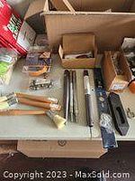 Wooden-handled brushes, metal components, and other assorted tool parts laid out on a surface