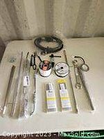 Photo of assortment of metal rods, clamps, welding rods in boxes, welding wire spool, and black paracord coil on table