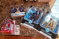 Four sealed action figures on a countertop: Spider-Man Venom, Transformers Optimus Prime, DC Multiverse Wonder Woman, and Batman.