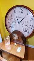 Large Eddie Bauer 25-inch wall clock with two smaller dials, standing on the floor against a yellow wall