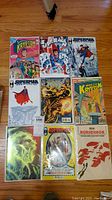 Photo showing 9 DC Comics comic books on wooden floor, including Superman, Krypton Chronicles, Catwoman, and Rorschach titles arranged in three rows and three columns.