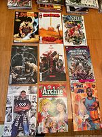 Top-down photo showing 10 comic books arranged in two rows on a wooden floor. Titles include Shazam, Superman, Steel, Batman Fortnite Zero Point (2 issues), Multiverse Who Laughs, a black male character comic, Archie Christmas Special, and Space Jam.
