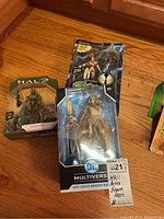 Lot of three unopened action figures including Halo, DC Multiverse, and Spawn figures on wooden surface.