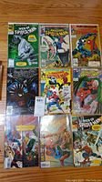 Top-down photo showing all 10 comic books laid out in two rows of five on a wooden floor. Covers visible featuring Spider-Man in various suits and battles, including black suit and armor suit.