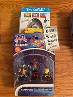 Photo showing unopened Bandai Tamagotchi virtual pet in white and pink packaging and Space Jam: A New Legacy stampers pack with three characters.