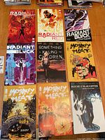 Nine comic books laid out on a wooden surface, showing titles Radiant Red, Radiant Black, Monkey Meat, Something is Killing the Children, House of Slaughter.