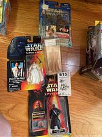 Photo showing all four Star Wars action figures in unopened packaging arranged on a wooden floor: Princess Leia Organa, Darth Maul, Chewbacca, and Obi-Wan Kenobi.