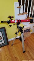 Full view of the red iOptron telescope mounted on tripod positioned near a yellow wall, showing the entire setup and placement.