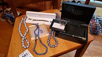 Full view of assorted jewelry items, including Kartens jeweled bracelet, three Asian ceramic bead necklaces, ceramic bead earrings, and L & Co. watch/pen/wallet set on table.