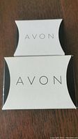 Two Avon branded boxes, one small and one larger, used to house the jewelry items.