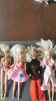 Four vintage Barbie dolls with blond hair in varying outfits and conditions, displayed on a mat.