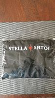 Black packaged Stella Artois BBQ apron in plastic wrapping with logo visible