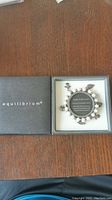 Fresh water pearl bracelet with multiple silver-tone charms inside branded Equilibrium box on wooden surface.
