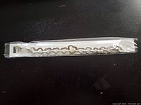 Gold tone heart shaped link bracelet sealed in plastic sleeve on dark surface.