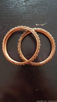 Two copper bangles with detailed beadwork and floral motifs on a dark surface
