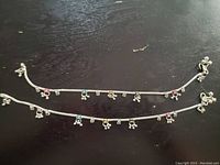 Two silver-tone chain anklets with multiple small colored bead charms spaced along each chain and lobster clasp closures.