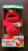 Front view of red Elmo plush toy in original green and white Tyco Sesame Street box with colorful text and a TRY ME tag attached.
