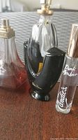 Photo showing three assorted fragrance bottles including Paloma Picasso, Pink Amber by Candie's, and a black perfume bottle on wooden surface