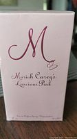 Close-up photo of Mariah Carey's Luscious Pink Eau de Parfum box front showing brand and product name in maroon script on pale pink background.