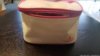 Closed cream and pink zippered carry bag with Conair branding seen on front.