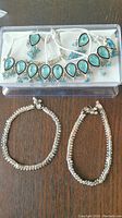 Photo of full necklace with blue teardrop stones, pair of matching earrings, and two silver bead anklets with hints of color