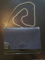 Front view of the vintage Pierre Cardin handbag showing textured exterior, metal Pierre Cardin logo on bottom corner, and silver chain strap arranged on dark surface.