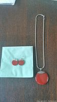Photo showing the red circular earrings with silver hooks and silver necklace with red pendant on a green cloth