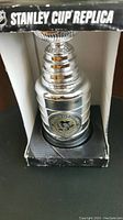 Close up image of the silver-tone Stanley Cup replica with Pittsburgh Penguins logo medallion on base inside original box.