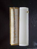 Bracelet inside its open rectangular box with light-colored inner lining, displaying the alternating silver and gold-tone links with a central flat plate for engraving.